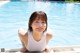 A woman in a white tank top leaning on the edge of a swimming pool.