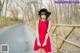 A woman in a red dress and black hat standing on a bridge.