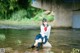 A woman in a school uniform sitting on a rock in the water.